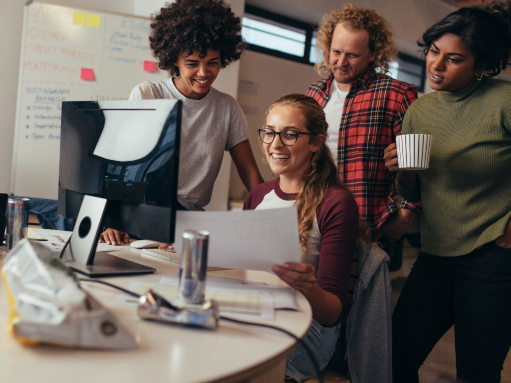 A group of young adults working at a fem-tech startup, sitting around a computer looking at paperwork.