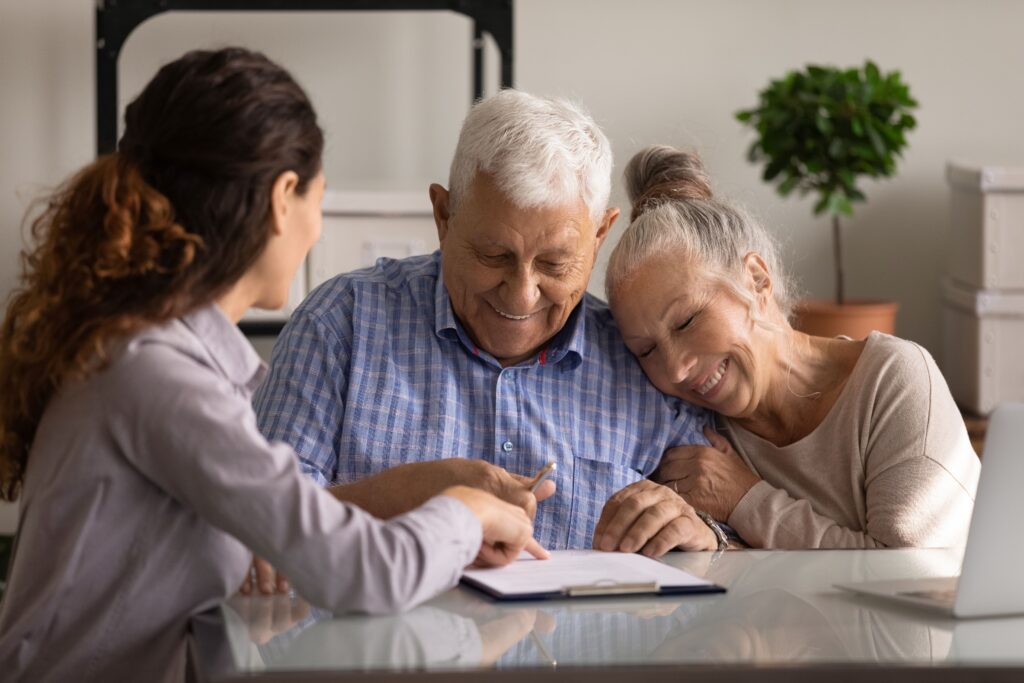 An older white couple meeting with a woman. They are looking at paperwork, smiling.