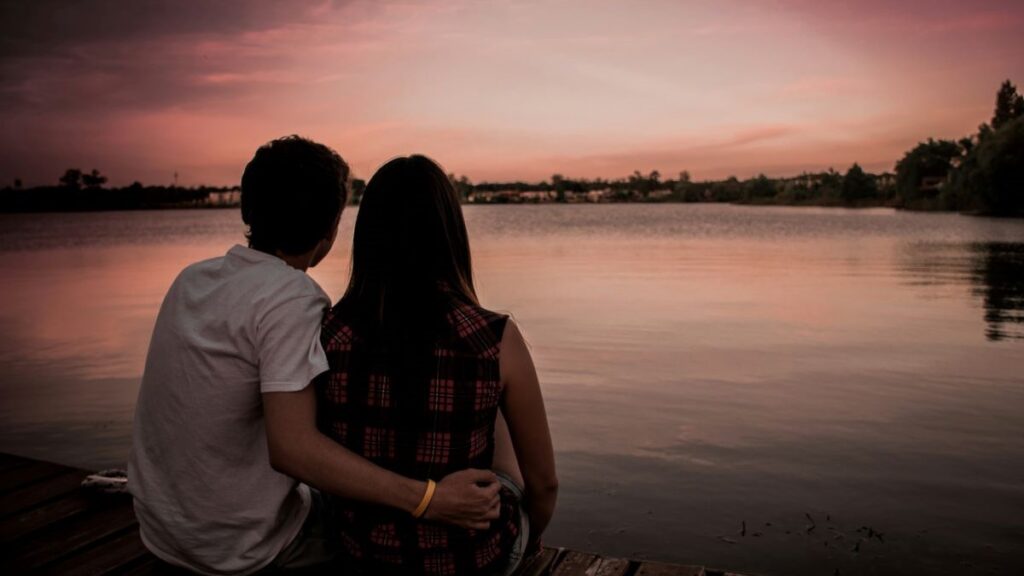 couple at the beach looking at a sunset and holding each other with affectionate touch