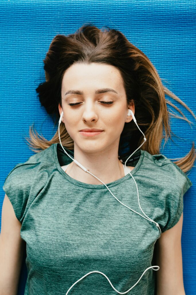 A woman is laying down on a blue blanket, she looks peaceful listening to something on headphones.
