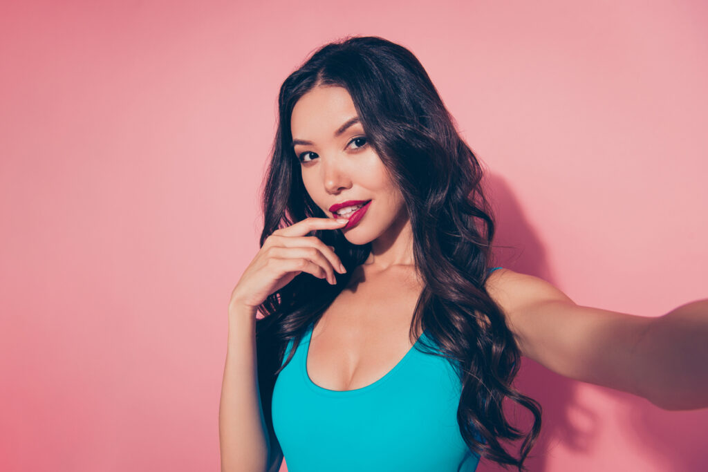 Young attractive brunette female doing a selfie in front of a pink background.