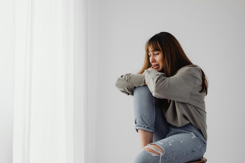 young woman sitting alone and sad. She has one knee propped up that she's resting her head on.